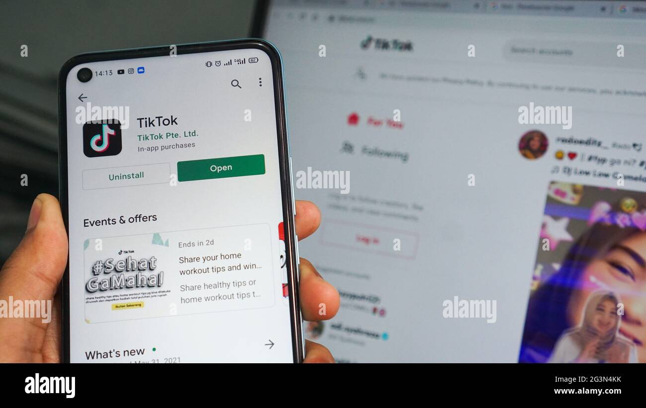 Dumai, indonesia - Giugno 17,2021: La mano dell'uomo asiatico sta tenendo un telefono cellulare e sta aprendo l'app TIKTOK, con sfondo laptop Foto Stock