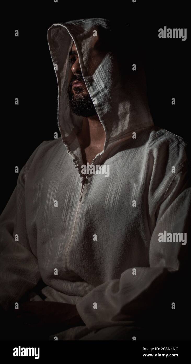 Un uomo musulmano africano con una barba che prega in un luogo buio e indossa una tradizionale djellaba marocchina bianca Foto Stock