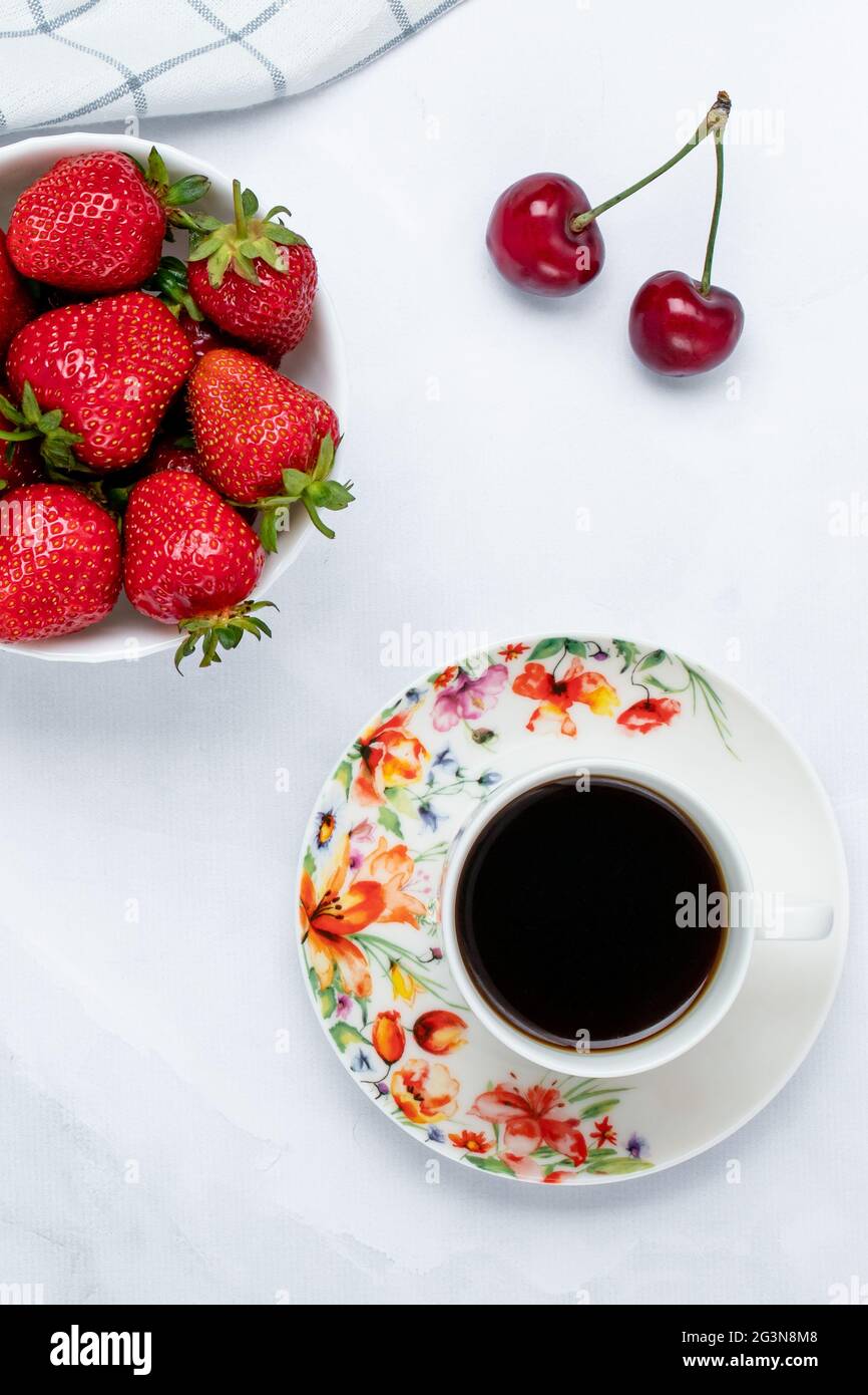 Una tazza di caffè nero e fragole su un tavolo bianco. Bevanda calda del mattino. Frutti di bosco rossi, concetto di colazione. Sfondo estivo, sfondo. Vege sano Foto Stock