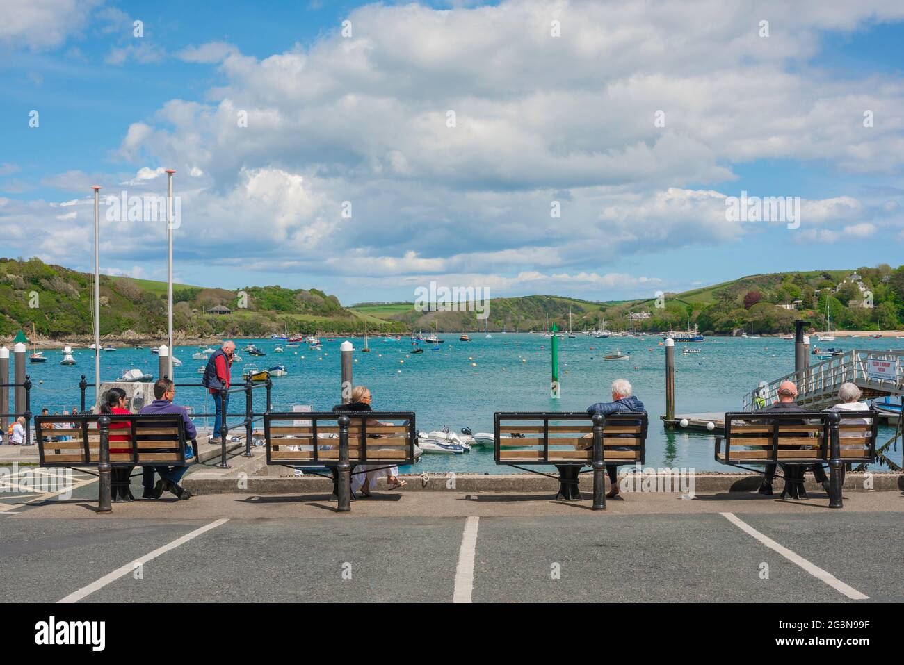 La gente porto, vista in estate di persone sedute su panchine nella zona del porto di Salcombe guardando verso l'estuario Kingsbridge, Devon, Inghilterra, Regno Unito Foto Stock