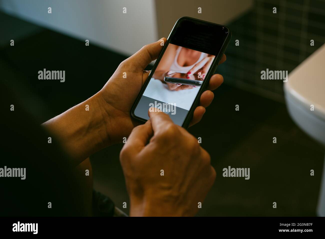 primo piano di un uomo caucasico, seduto in bagno, datando online nel suo smartphone, con una mock app nel suo schermo Foto Stock