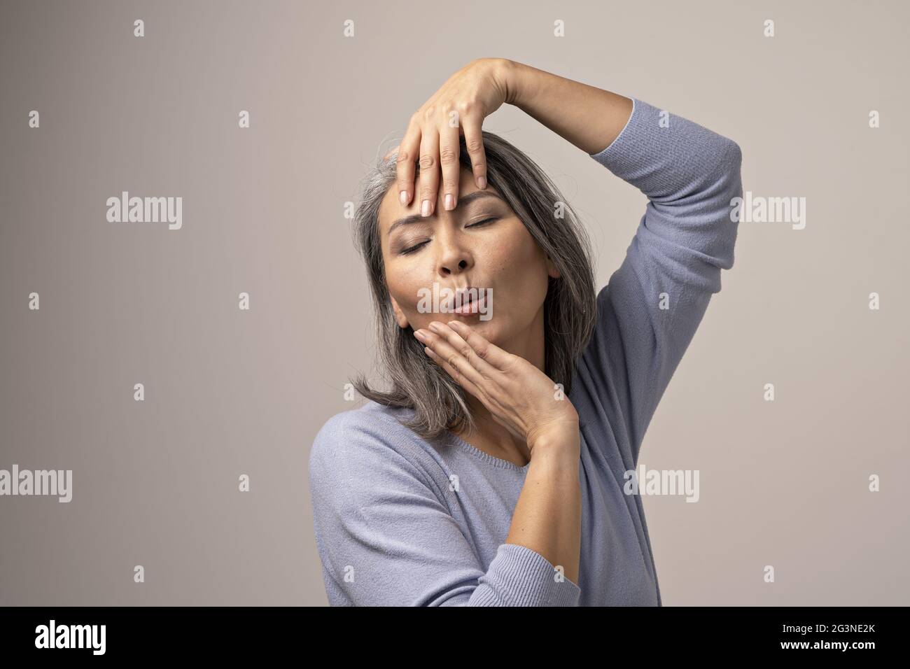 Attraente donna asiatica è emotivamente in posa di toccare la sua testa con le mani Foto Stock