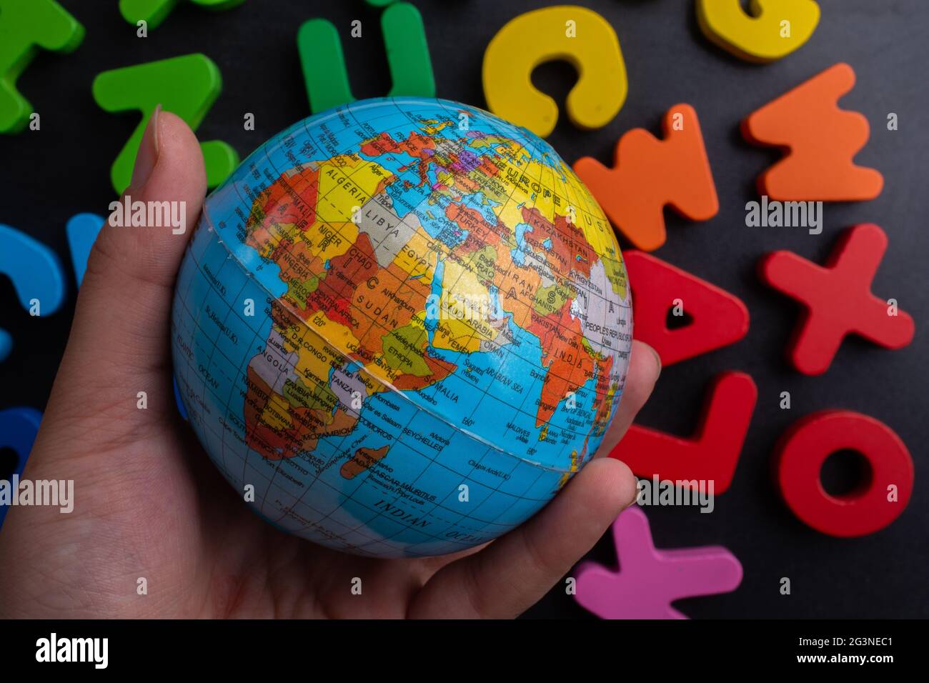 Mano che tiene un modello globo su lettere colorate su uno sfondo nero Foto Stock