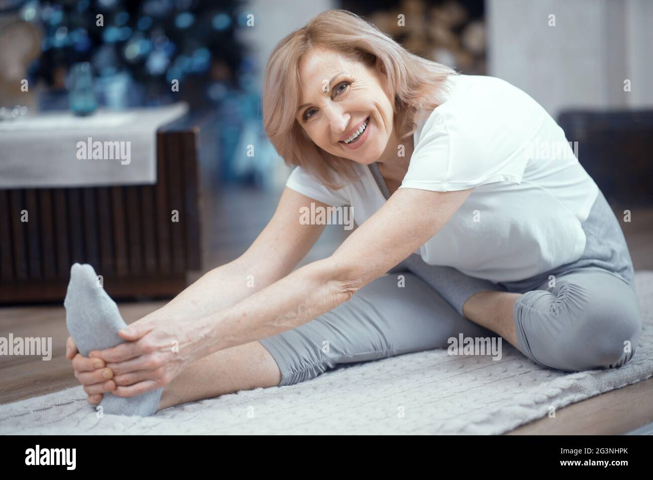 Sorridente donna matura sta toccando le dita dei piedi Foto Stock