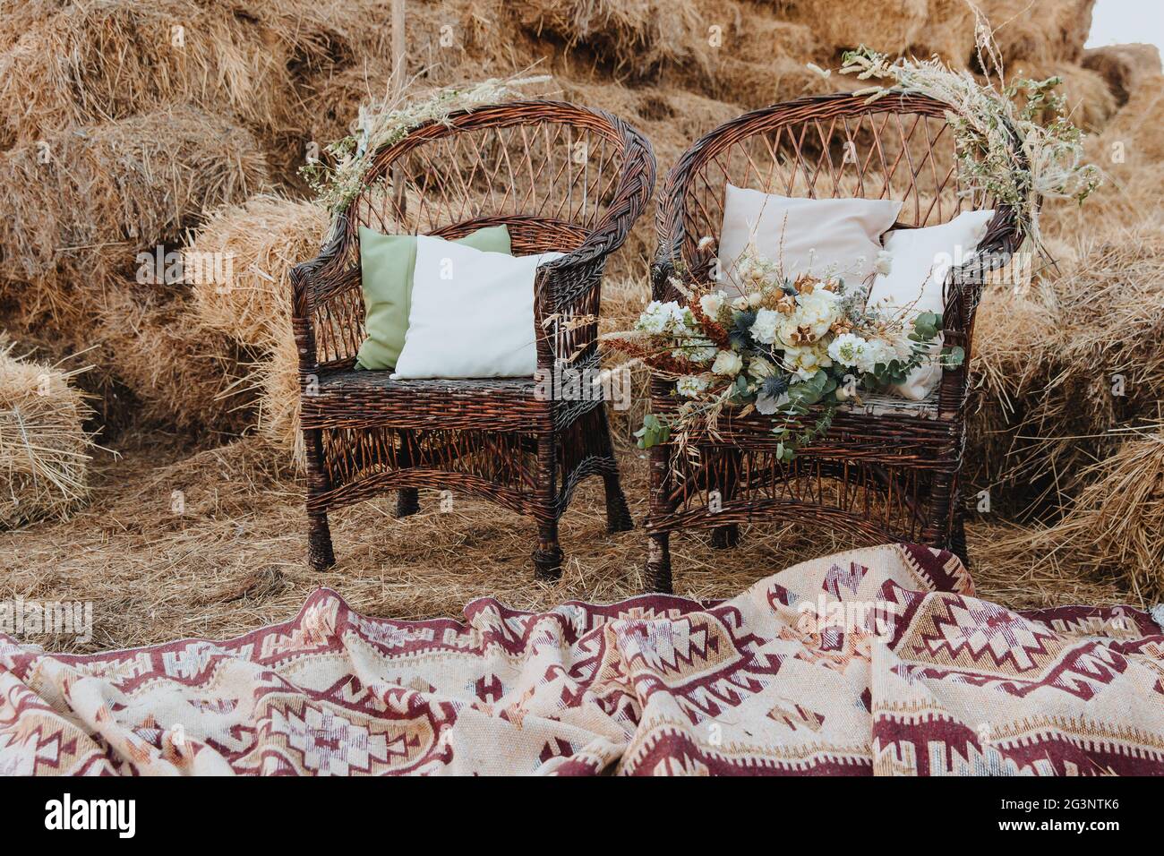 Due sedie in vimini con cuscini e un bouquet di fiori su di essa. Sedie in  rattan con balle di paglia sullo sfondo. Stile boho Foto stock - Alamy