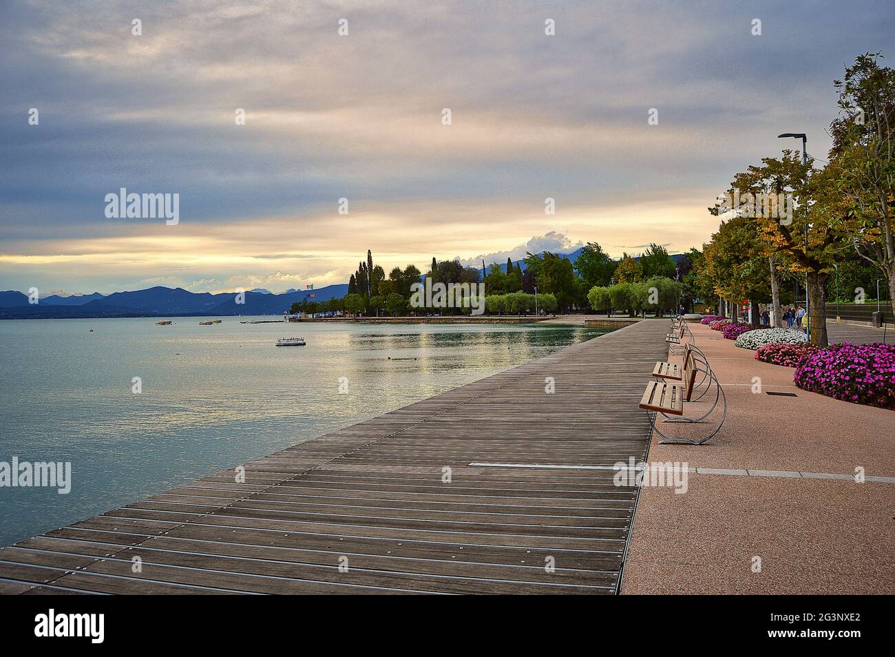 Lungomare molo di Bardolino, lago di Garda con panchine, fiori, alberi, acqua e suggestivo cielo serale Foto Stock