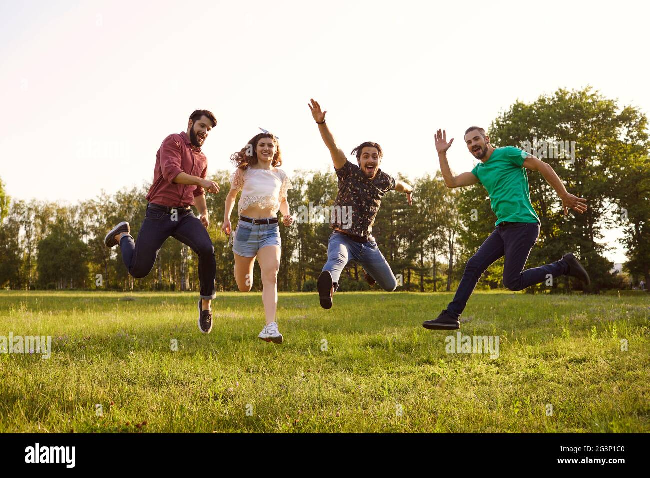 Felici giovani amici che saltano insieme all'aperto. Gruppo di persone che si divertono durante le vacanze estive in campagna Foto Stock