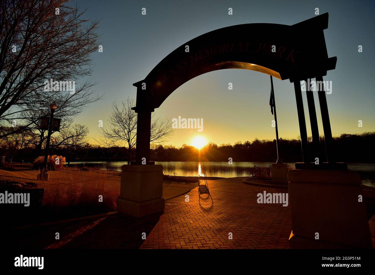Elgin, Illinois, Stati Uniti. Il tramonto si riflette sul fiume Fox visto attraverso l'arco del Veterans Memorial Park a Elgin, Illinois. Foto Stock