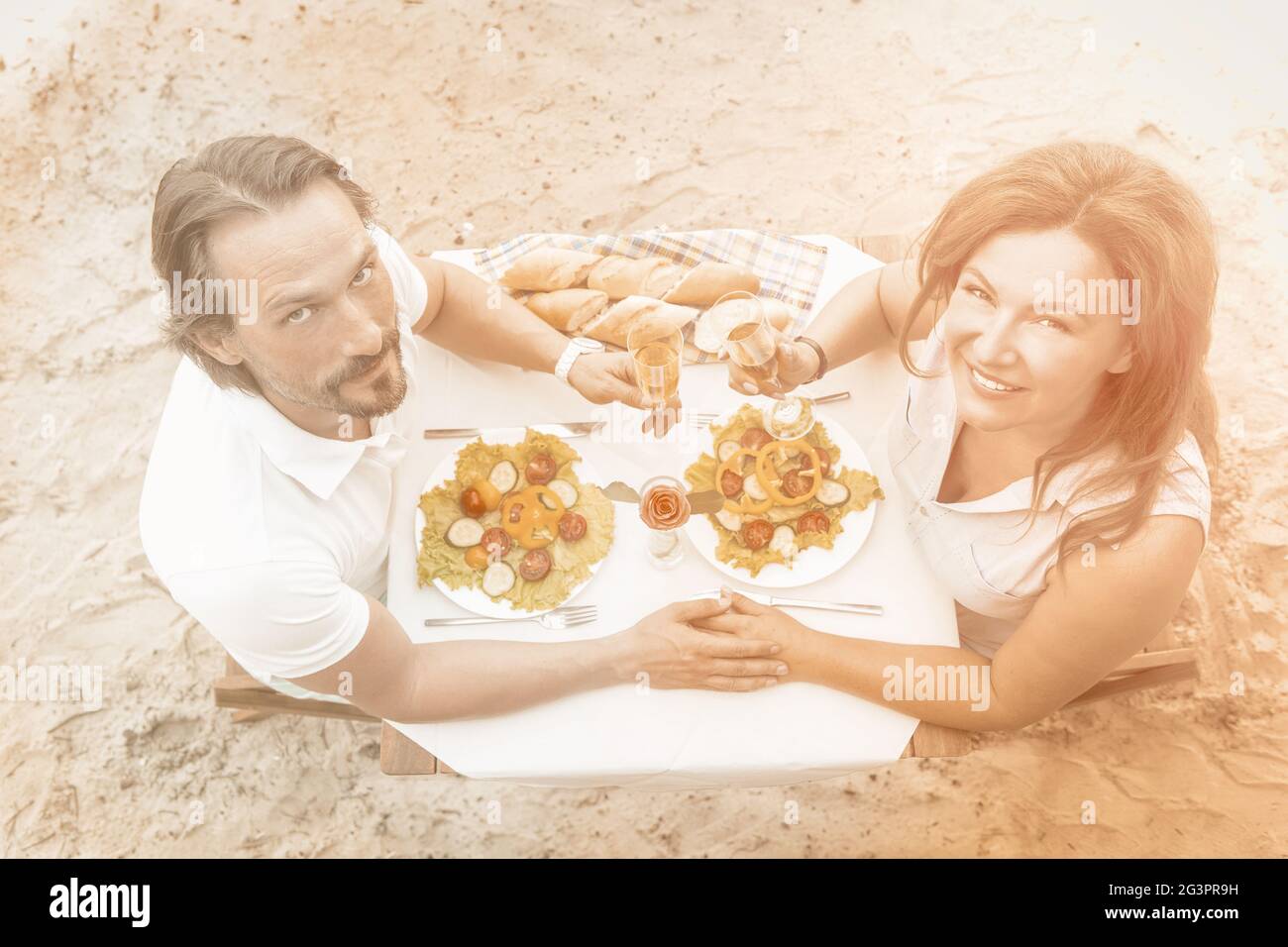 Le coppie mature hanno un evento all'aperto. L'uomo e la donna si siede tenendo nand alzando un bicchiere di vino o champagne contro lo sfondo Foto Stock