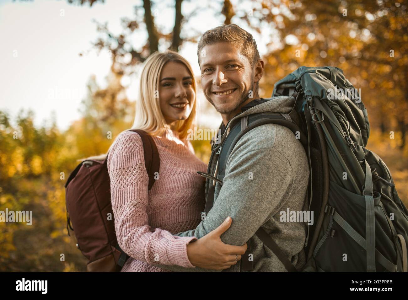 Happy backpackers in amore ride abbracciando mentre si guarda la macchina fotografica e in piedi contro lo sfondo della natura autunnale Foto Stock