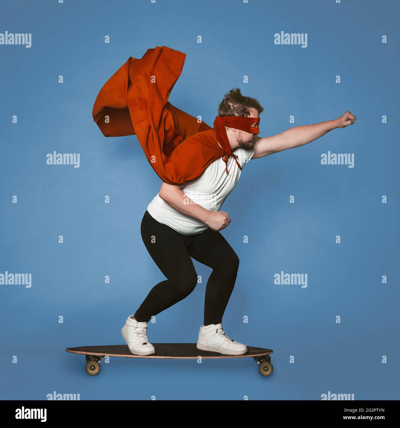 Concetto di Super Speed. Supereroe si lancia in avanti su uno skateboard. Uomo in costume rosso supereroe con un mantello volante isolato in dissolvenza Foto Stock