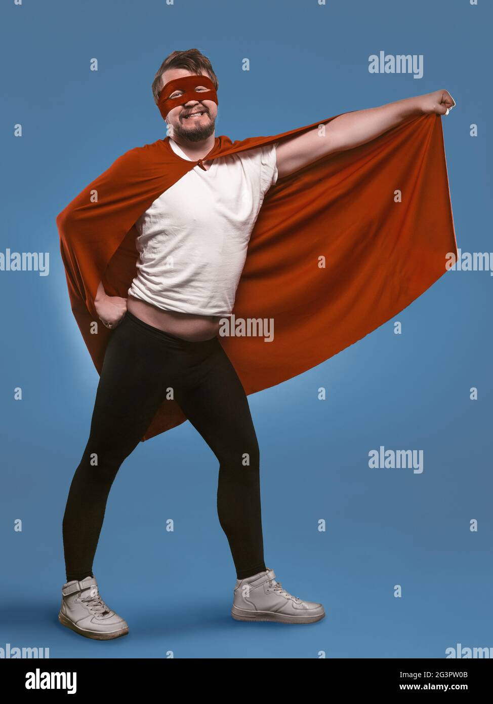 Uomo super eroe sorridente pronto a volare salvare mondo. Uomo divertente in costume rosso supereroe e maschera tenendo il suo mantello con la mano che poso io Foto Stock
