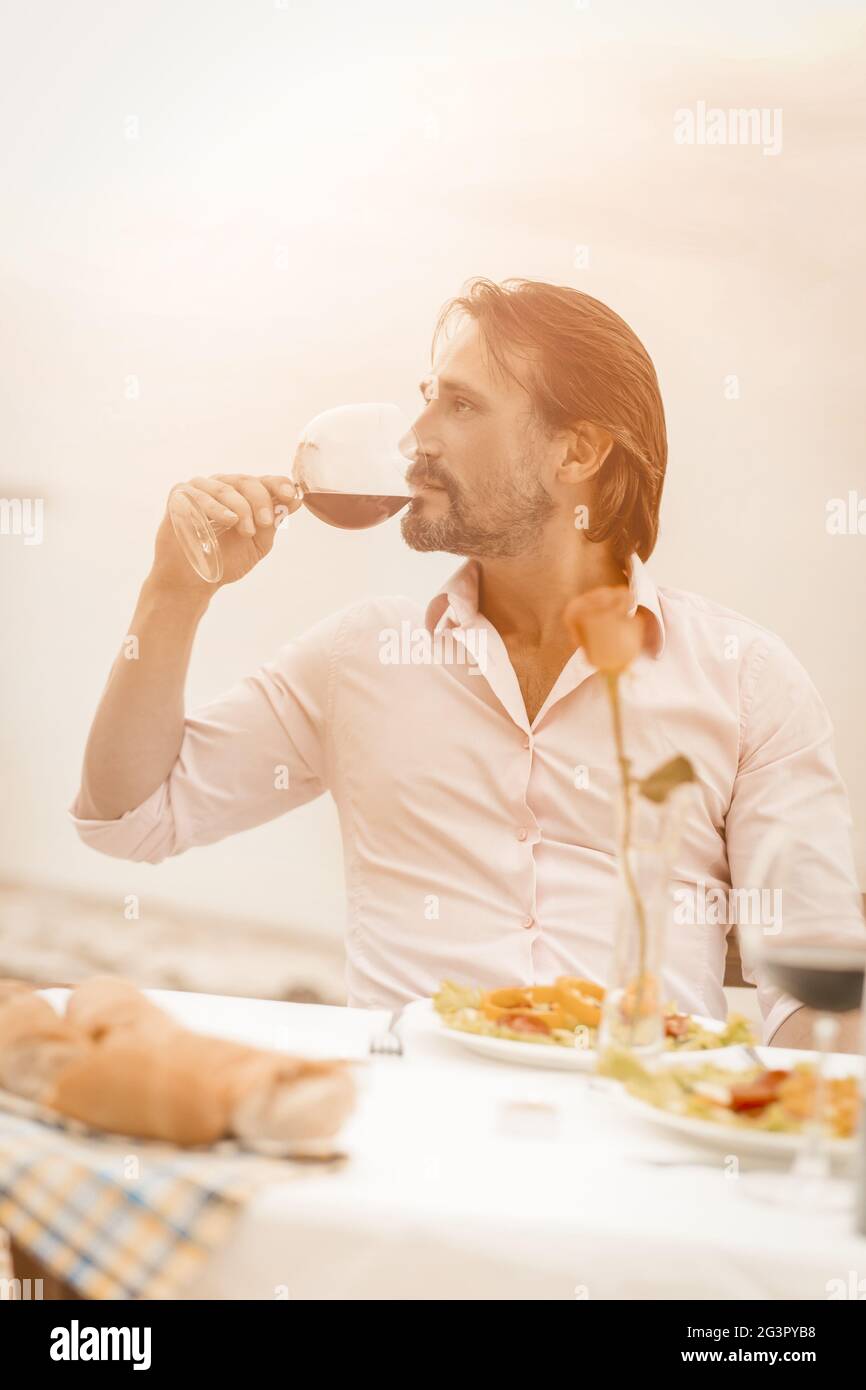 L'uomo caucasico beve vino di lusso all'aperto. Vista del profilo dell'attraente uomo di mezza età che gode di una bevanda meravigliosa mentre mi siede Foto Stock