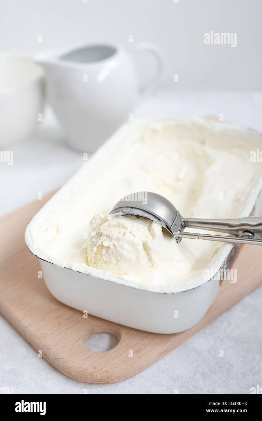 Palla gelato alla vaniglia fatta in casa in cucchiaio su contenitore gelato su sfondo bianco, concetto di cucina casalinga, primo piano. Foto Stock