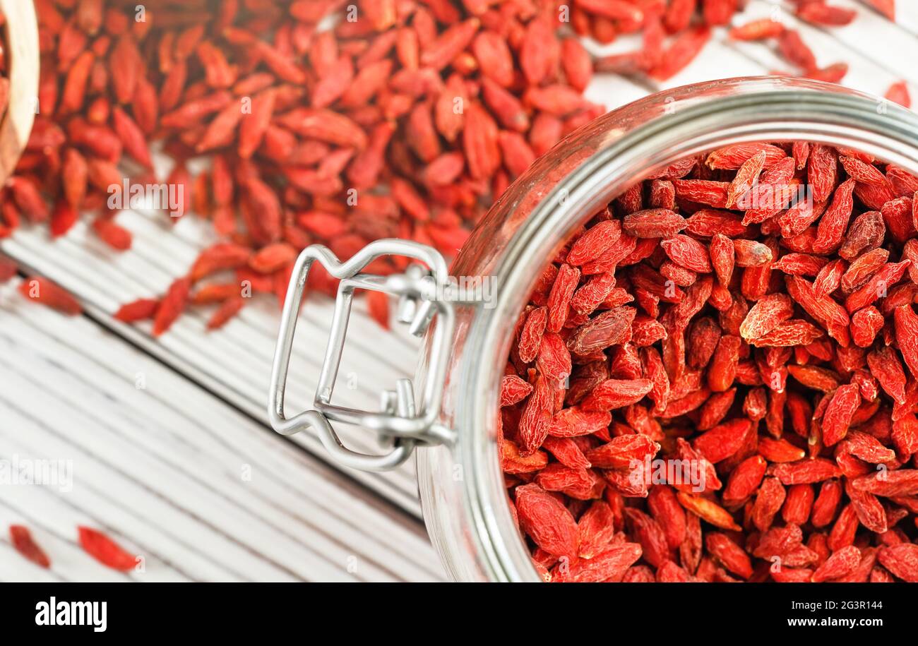 Goji secco aka. Semi di mirtillo all'interno di una bottiglia di vetro, alcuni sparsi su una scrivania di tavole bianche Foto Stock