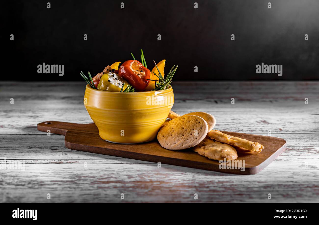 Fotografia scura di peperoni ripieni di formaggio cremoso. Antipasto estivo mediterraneo su tavola di legno con pane duro. Foto Stock
