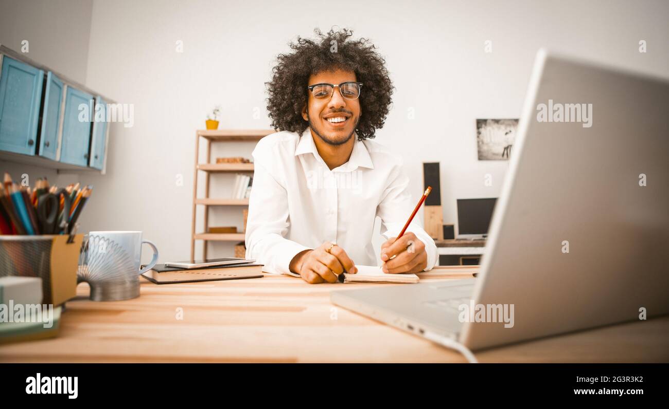 L'uomo freelance guarda la macchina fotografica che fa notare mentre lavora con il calcolatore. Vista frontale di un uomo d'affari giovane o millenario creativo Foto Stock