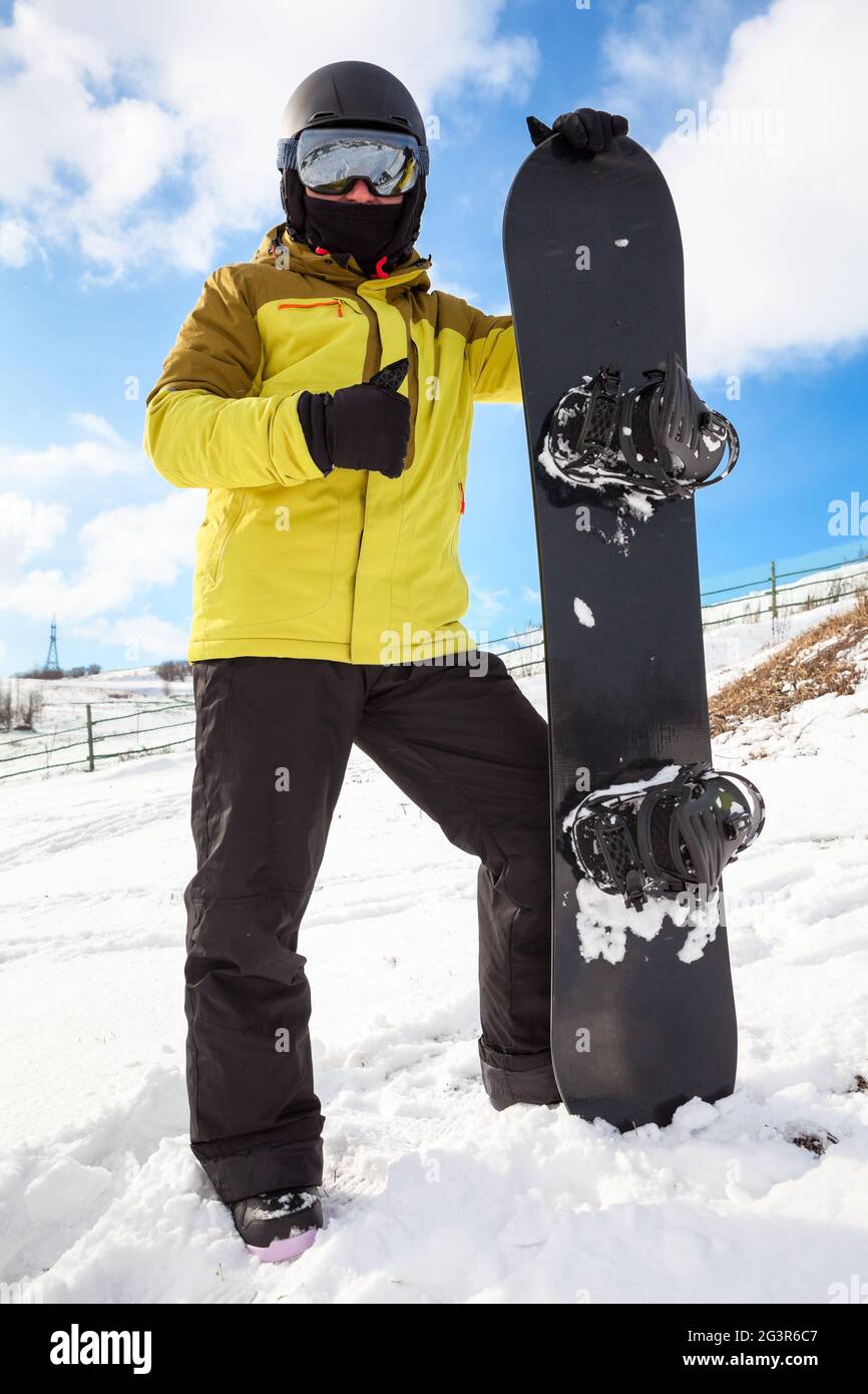 Uomo snowboarder con snowboard in piedi su pendii di montagna, tenendo la  sua tavola, indossando occhiali a specchio, pollice in su Foto stock - Alamy