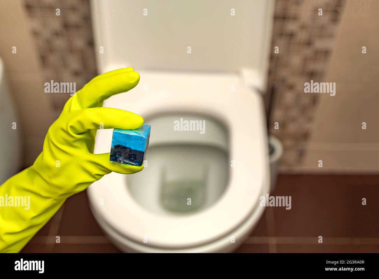 Detersivo a mano per i cubetti di gabinetto. Una mano abbassa un cubo disinfettante nell'acqua di una tazza igienica incorporata nella parete Foto Stock