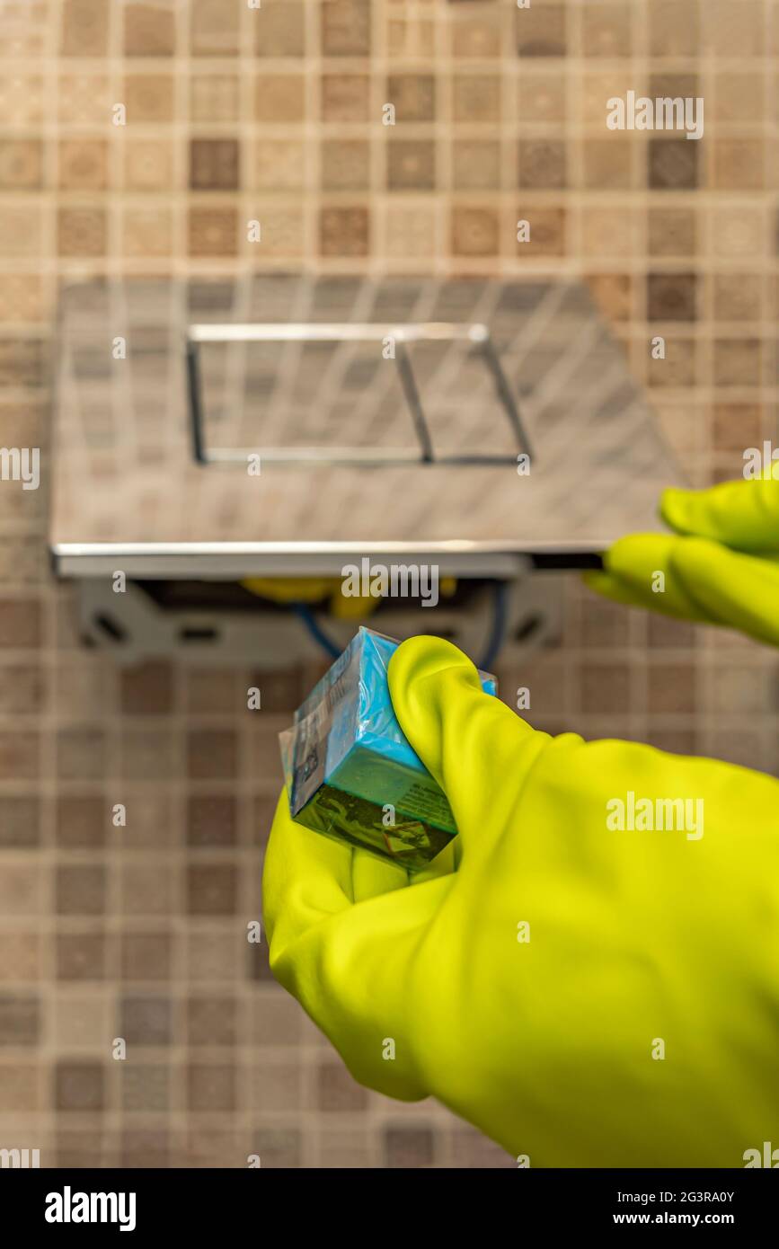 Detersivo a mano per i cubetti di gabinetto. Una mano abbassa un cubo disinfettante nell'acqua di una tazza igienica incorporata nella parete Foto Stock