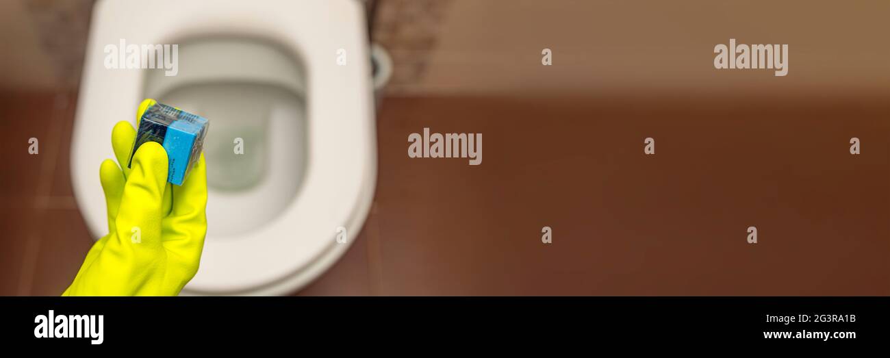 Detersivo a mano per i cubetti di gabinetto. Una mano abbassa un cubo disinfettante nell'acqua di una tazza igienica incorporata nella parete Foto Stock