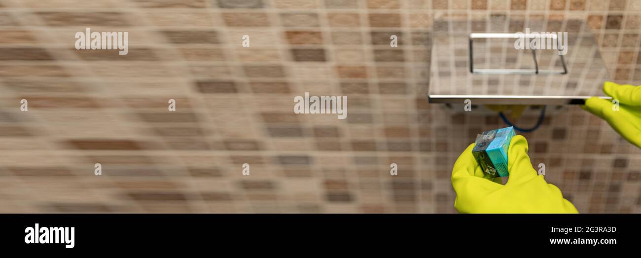 Detersivo a mano per i cubetti di gabinetto. Una mano abbassa un cubo disinfettante nell'acqua di una tazza igienica incorporata nella parete Foto Stock