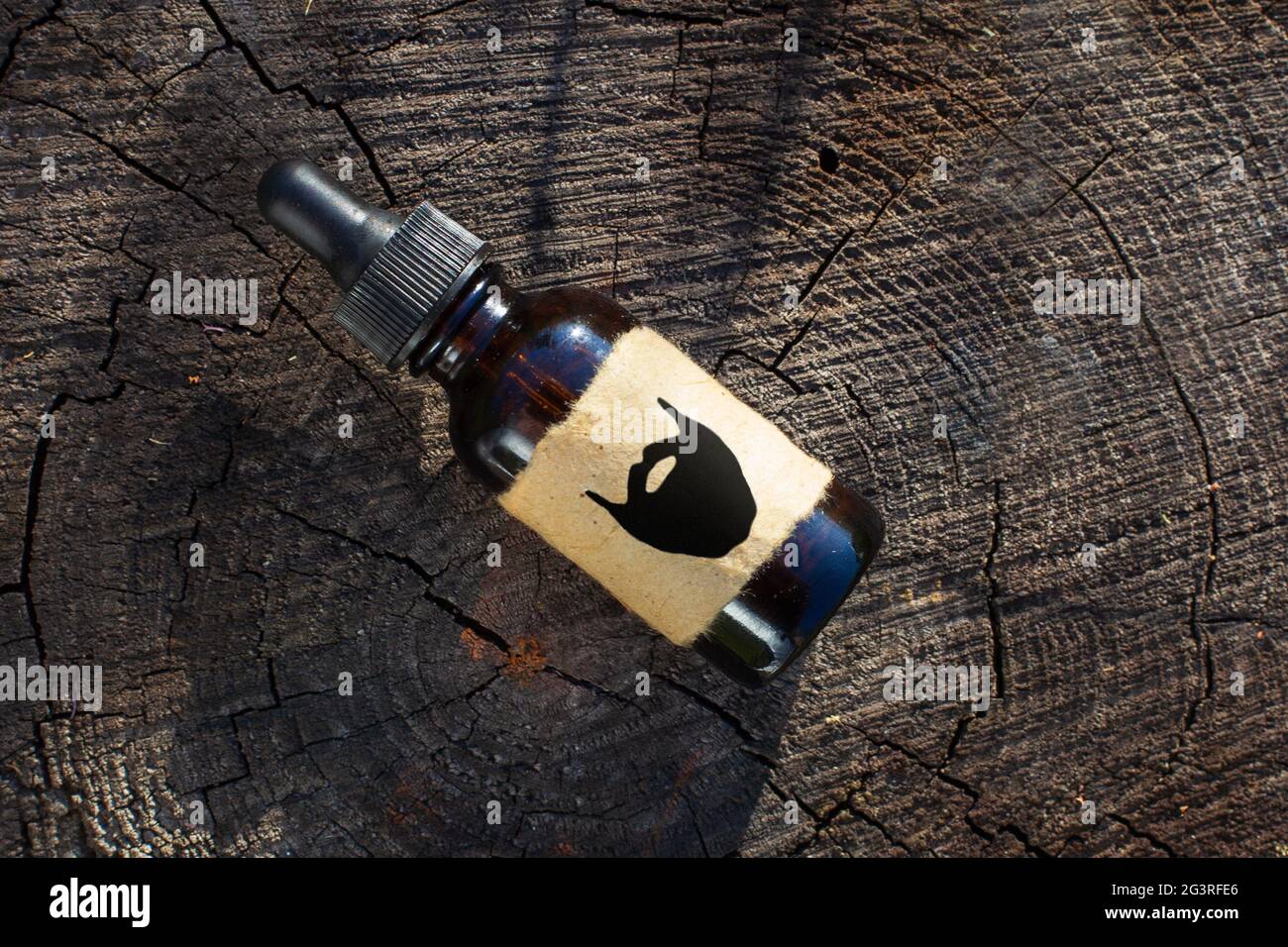 Olio per la cura e la crescita della barba, barbiere. Una bottiglia di estratto di barba su un vecchio tronco d'albero. Flatley Foto Stock