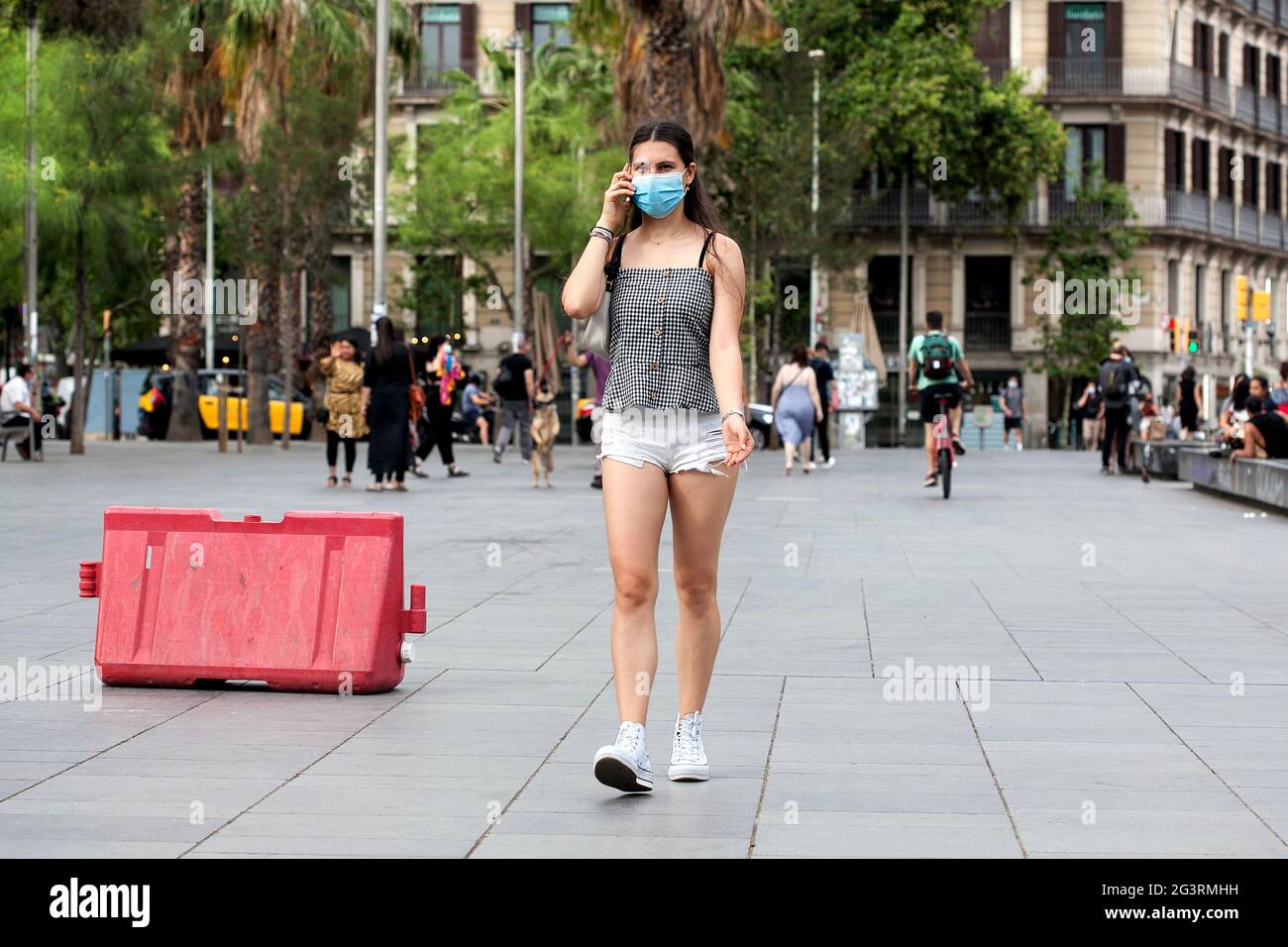 Giovane donna che indossa pantaloncini bianchi che cammina e parla al cellulare, Barcellona, Spagna. Foto Stock