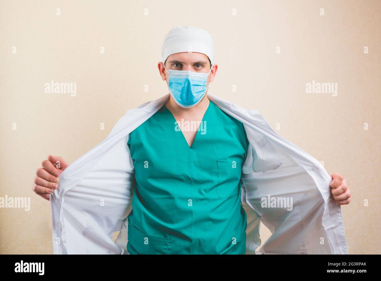 Medico in maschera medica protettiva e vestito verde apre il suo cappotto bianco isolato Foto Stock