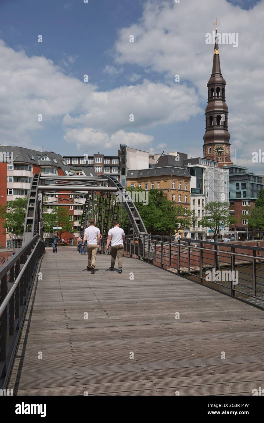 Persone che attraversano il ponte e la vita cittadina ad Amburgo in Germania con la chiesa di Santa Caterina sullo sfondo Foto Stock