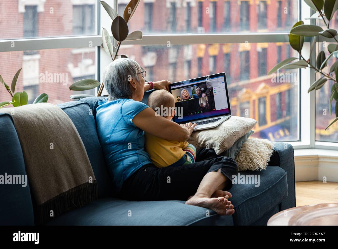Donna anziana seduta con la nipote che effettua una videochiamata attraverso il computer portatile in soggiorno a casa Foto Stock