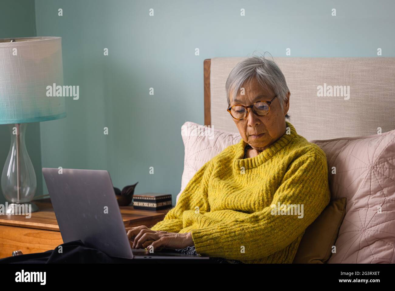 Donna anziana che usa il computer portatile mentre si siede in camera da letto a casa Foto Stock