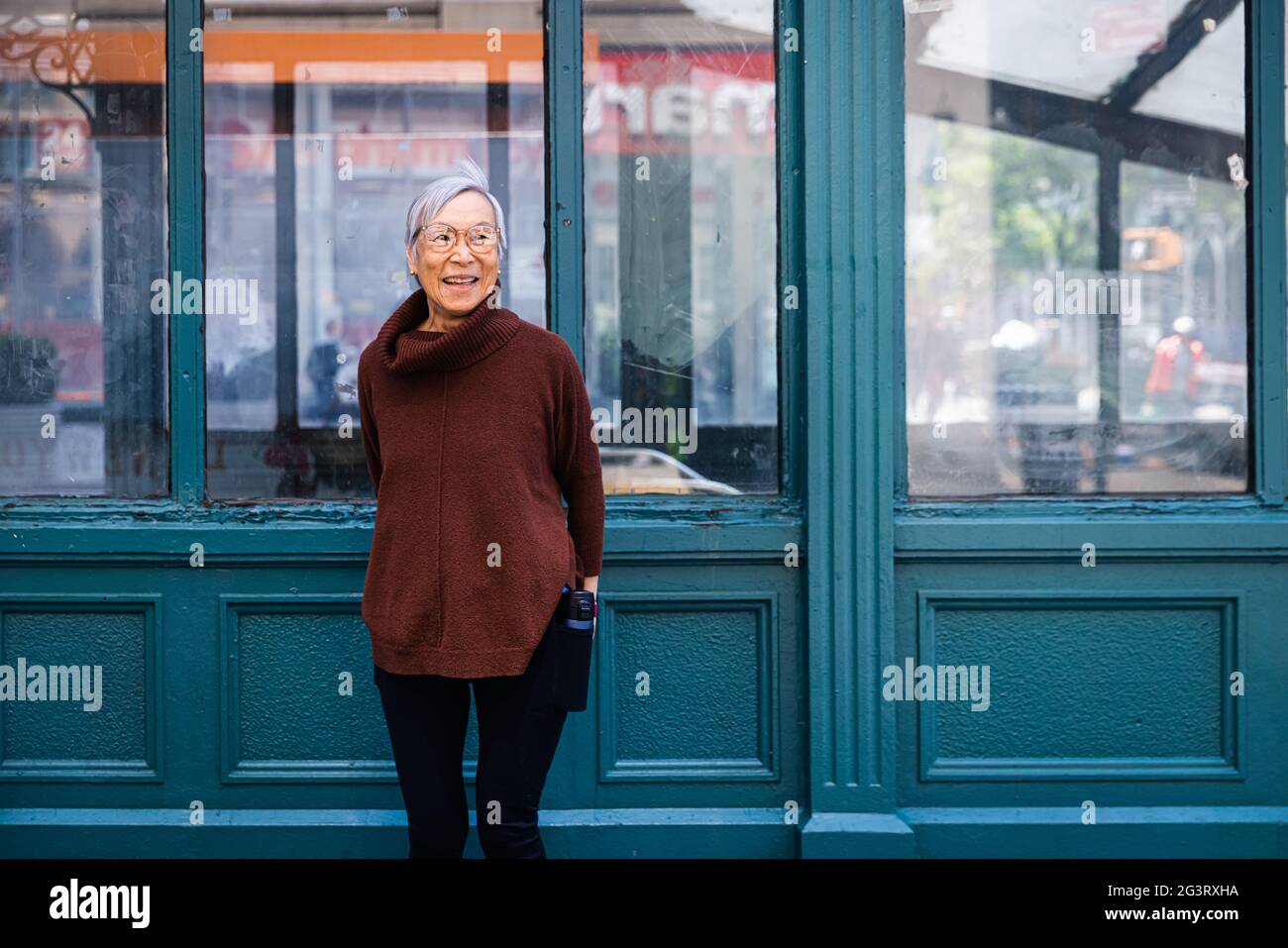 Donna anziana felice che guarda via mentre si sta contro il muro Foto Stock