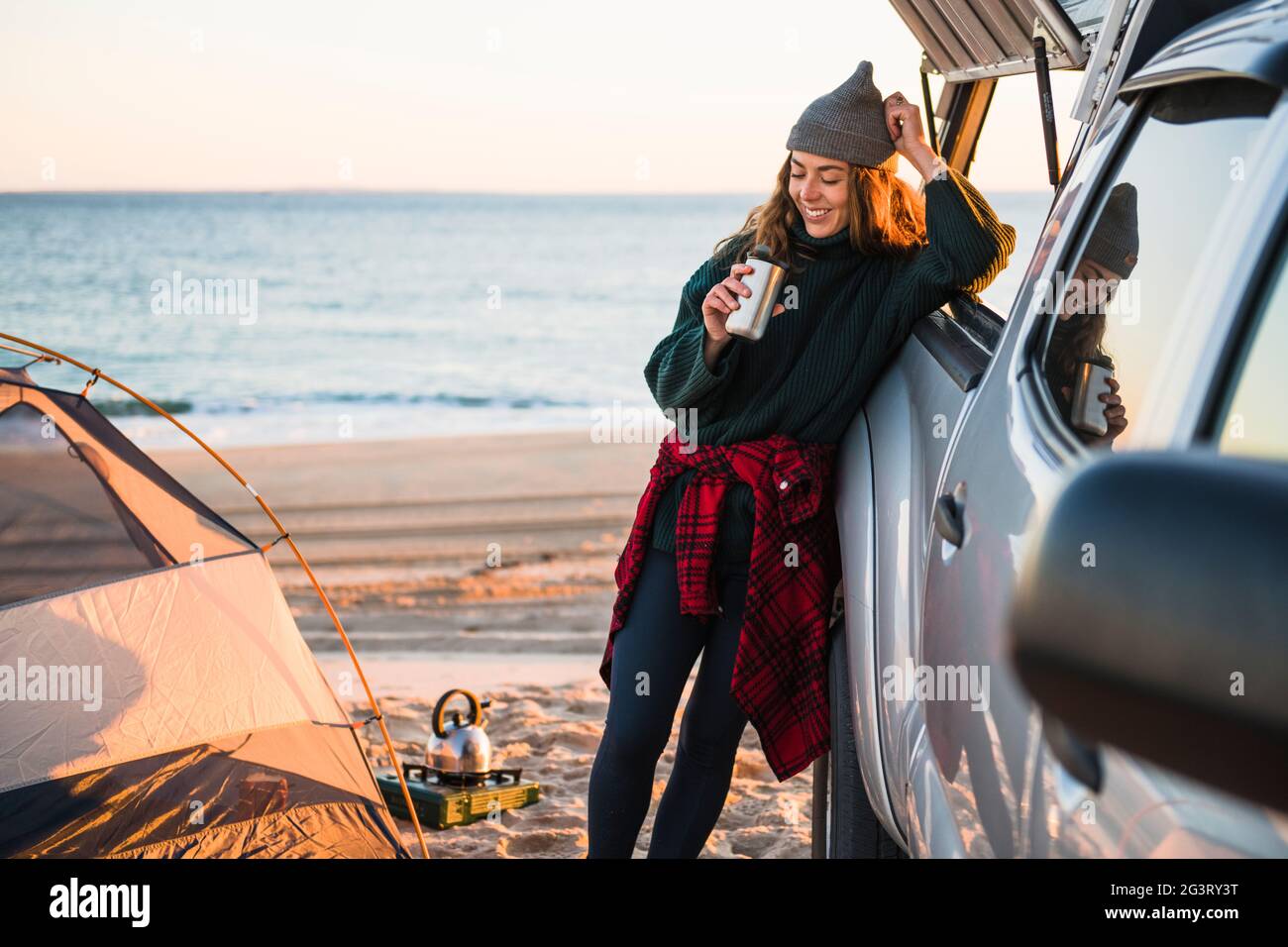 Giovane donna che ama il caffè nella tazza da viaggio mentre si accampano le auto da spiaggia Foto Stock