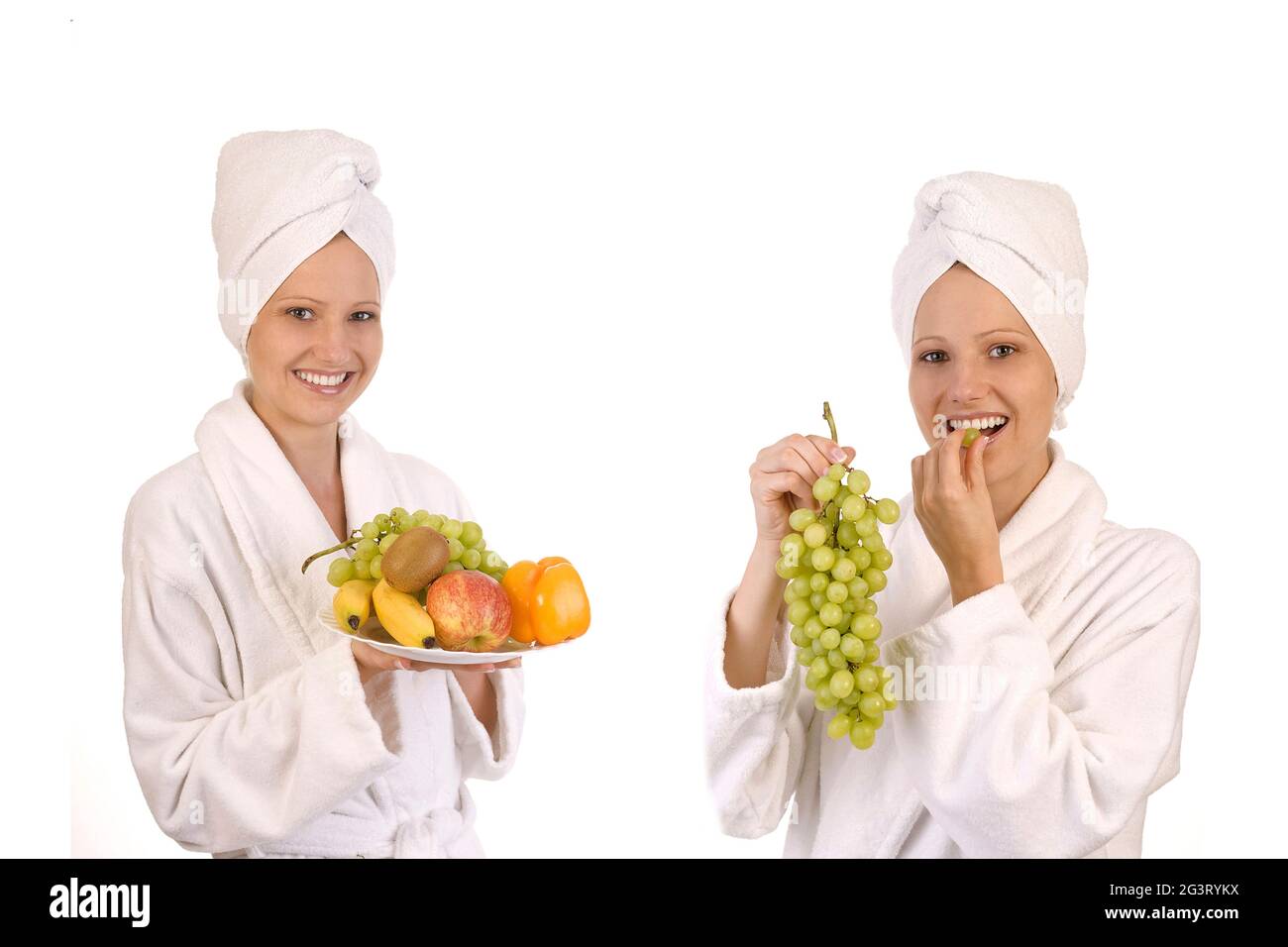 due giovani donne in accappatoi bianchi che mangiano uva e frutta Foto Stock