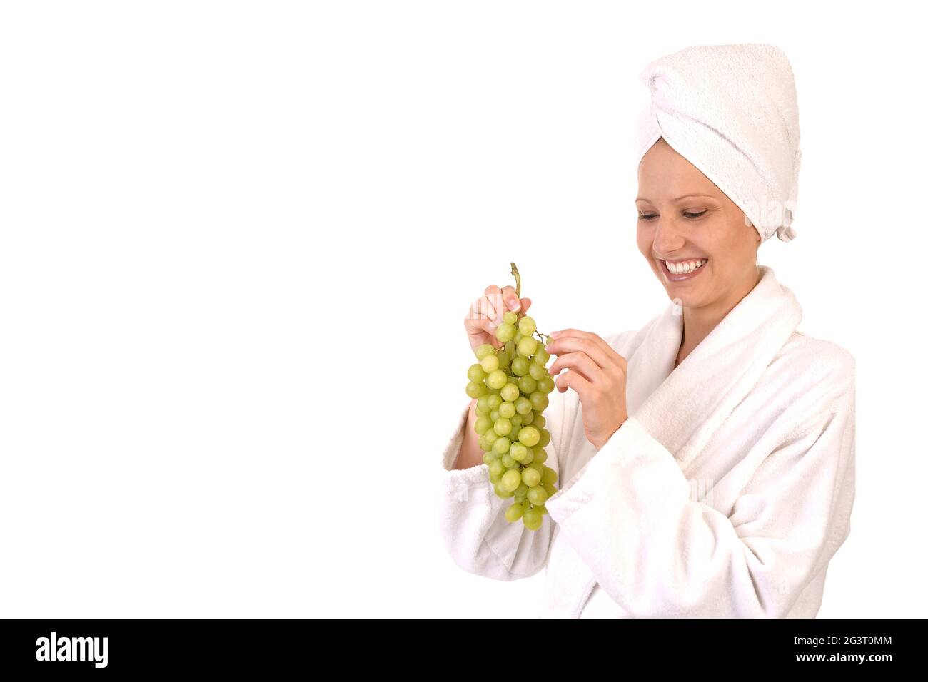 giovane donna in accappatoio bianco che mangia uva Foto Stock