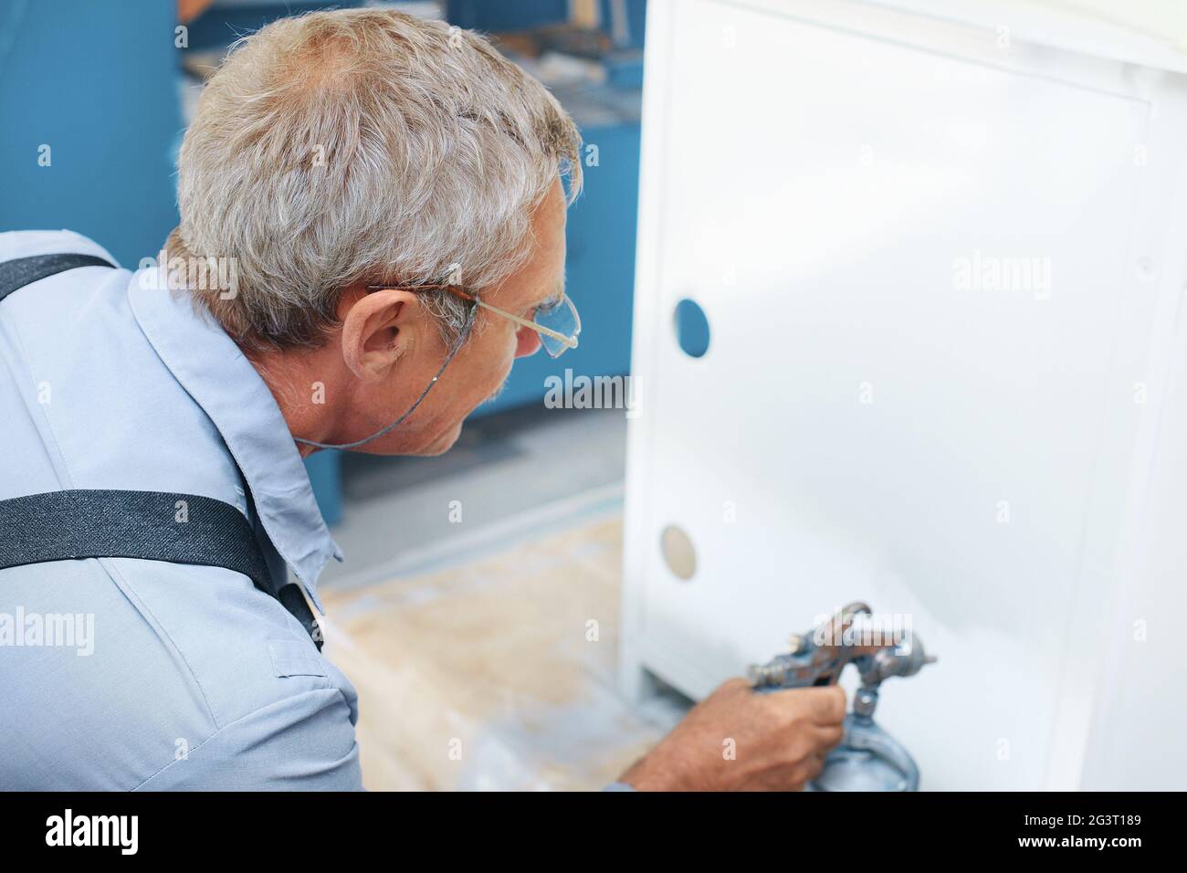 Un dipendente dipinge i prodotti metallici. Un uomo anziano tiene una pistola a spruzzo a compressore in mano e vernice Foto Stock