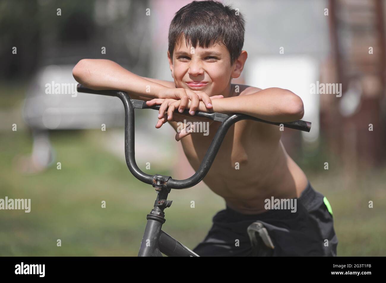 Un bambino con una vecchia bicicletta sulla strada. Un ragazzo bianco si siede su una bicicletta obsoleta in una giornata estiva. Foto Stock