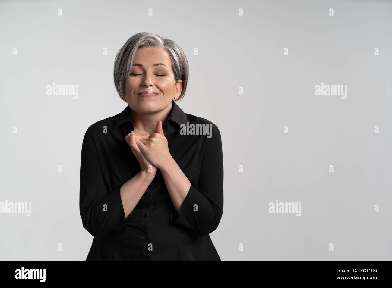 Donna matura felice ha piegato le mani con gli occhi chiusi su sfondo bianco. Concetto dei sogni. Concetto di emozioni Foto Stock