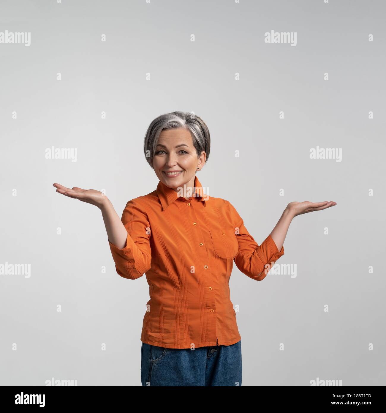 Donna felice sorpresa guardando con la bocca aperta tenendo le braccia fuori. Ritratto di felice donna matura allegra in blusa arancione Foto Stock