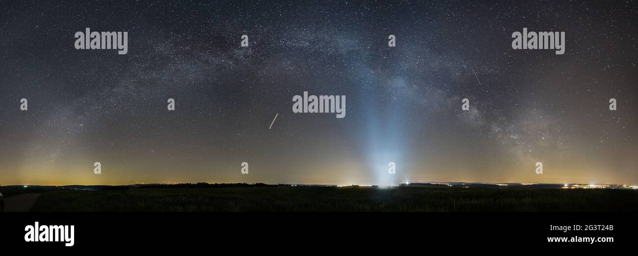 Panorama della Via Lattea inchino sul paesaggio rurale con le luci della base aerea di Spangdahlem in distanza, Germania Foto Stock