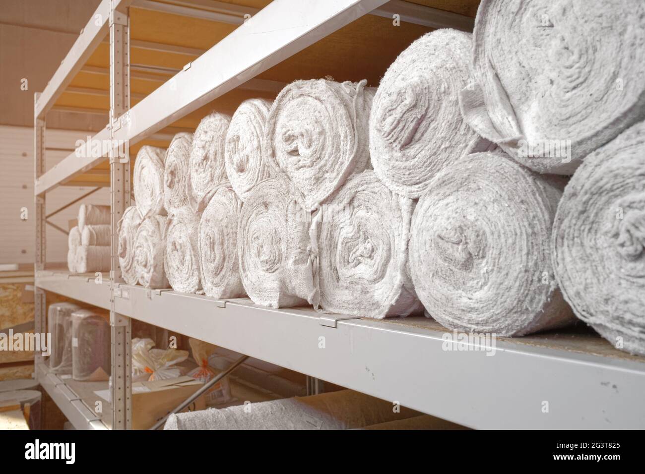 Il materiale bianco in rotoli si trova sui ripiani del magazzino. Materiale di copertura. Tessili per la produzione di stracci. Foto Stock