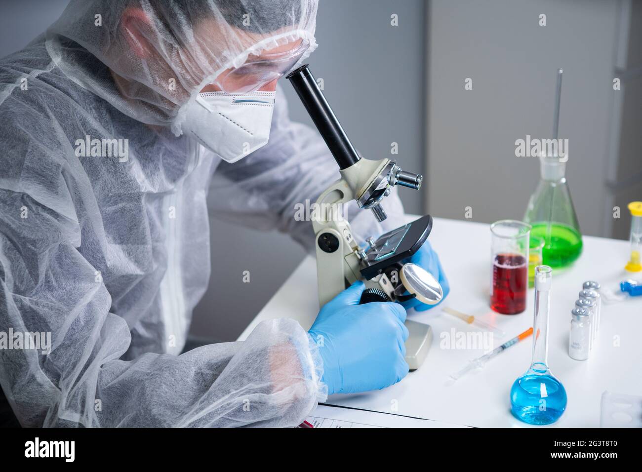 Scienziato che esamina il campione con un microscopio, facendo ricerca medica in laboratorio di scienza. Assistente di laboratorio maschile in Protect Foto Stock