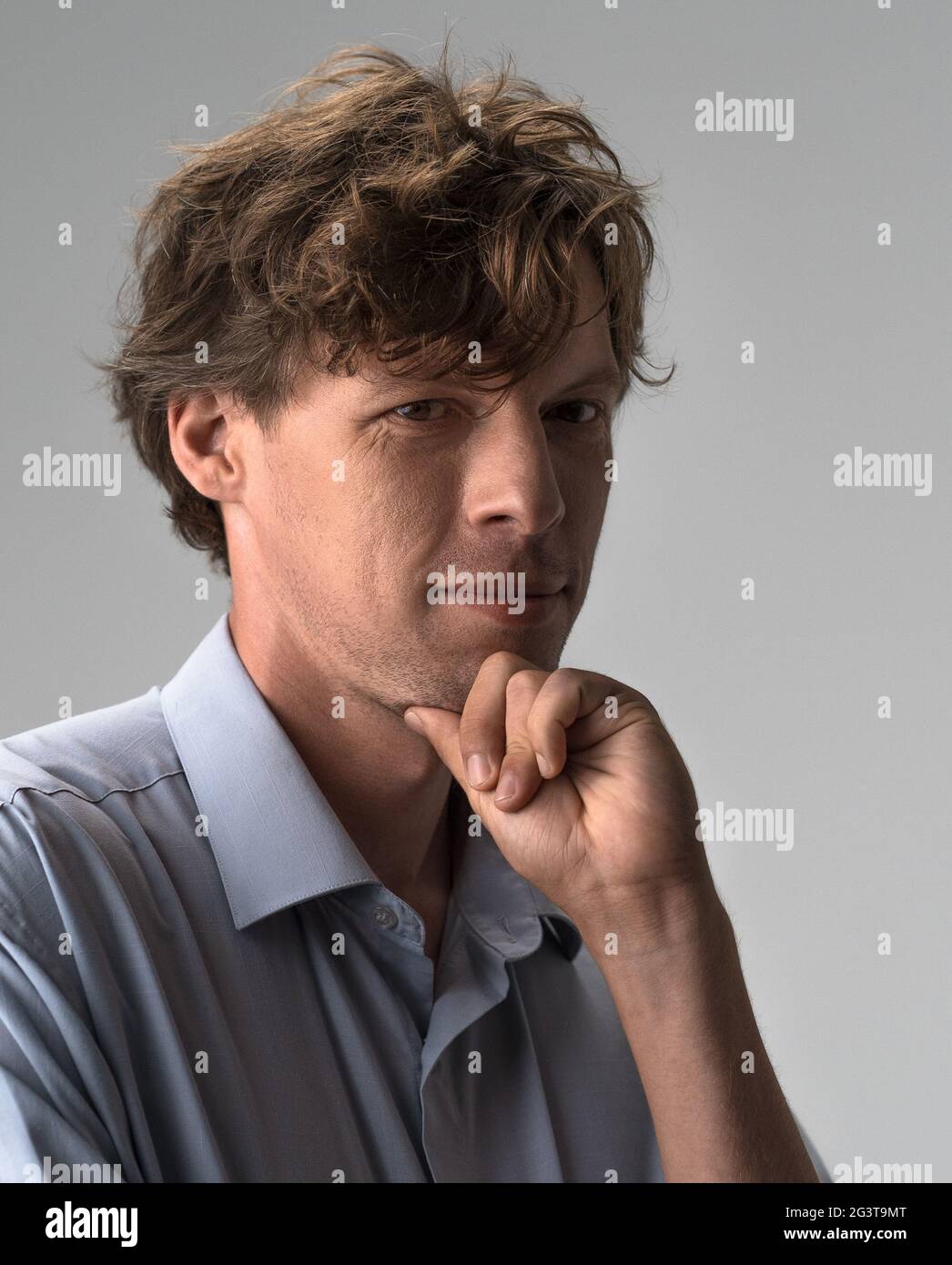 Ragazzo premuroso che si appoggia la mano, strofinando la barba mentre si pensa alla scelta difficile, studio interno girato isolato su bianco o luce g Foto Stock