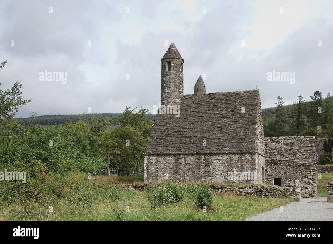 Torre rotonda in pietra e alcune rovine di un insediamento monastico originariamente costruito nel 6 ° secolo nella valle di Glendalough, County Wick Foto Stock