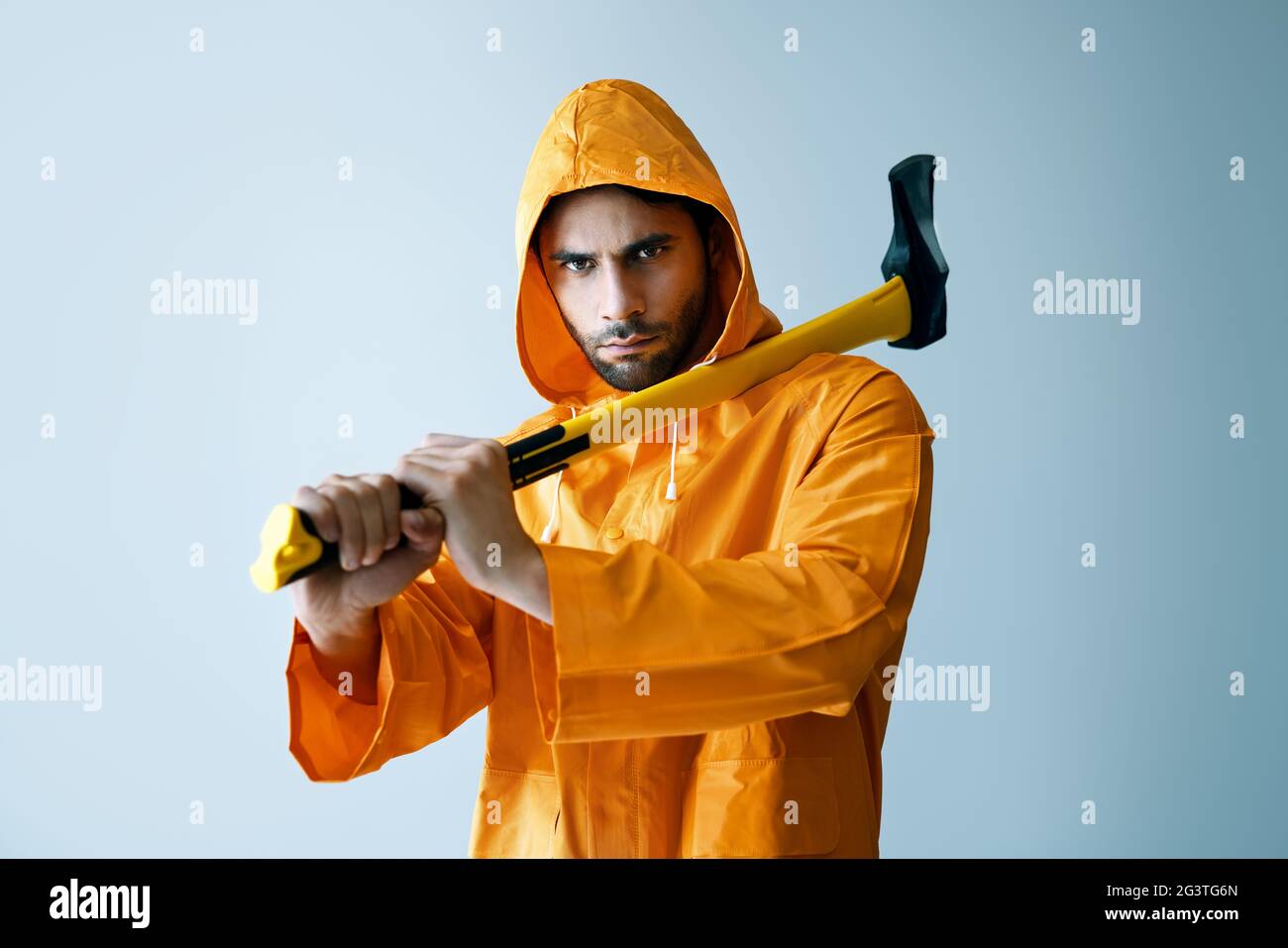 Giovane uomo serio in impermeabile luminoso che tiene grande ascia sulla spalla Foto Stock