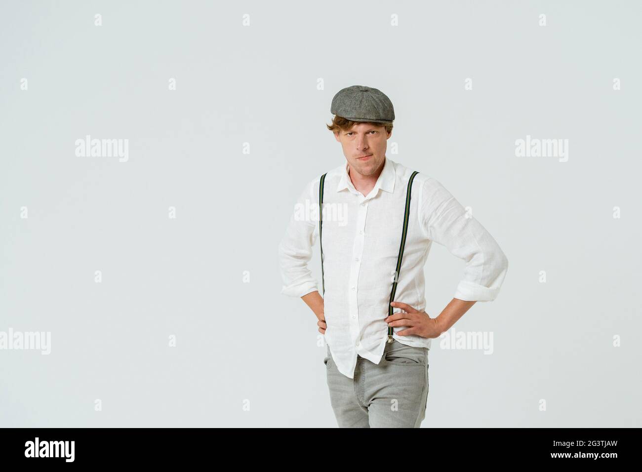 Bell'uomo hipster in posa con le mani sui fianchi vestiti di camicia bianca e jeans grigi e cappuccio di lana isolato su sfondo bianco. Foto Stock