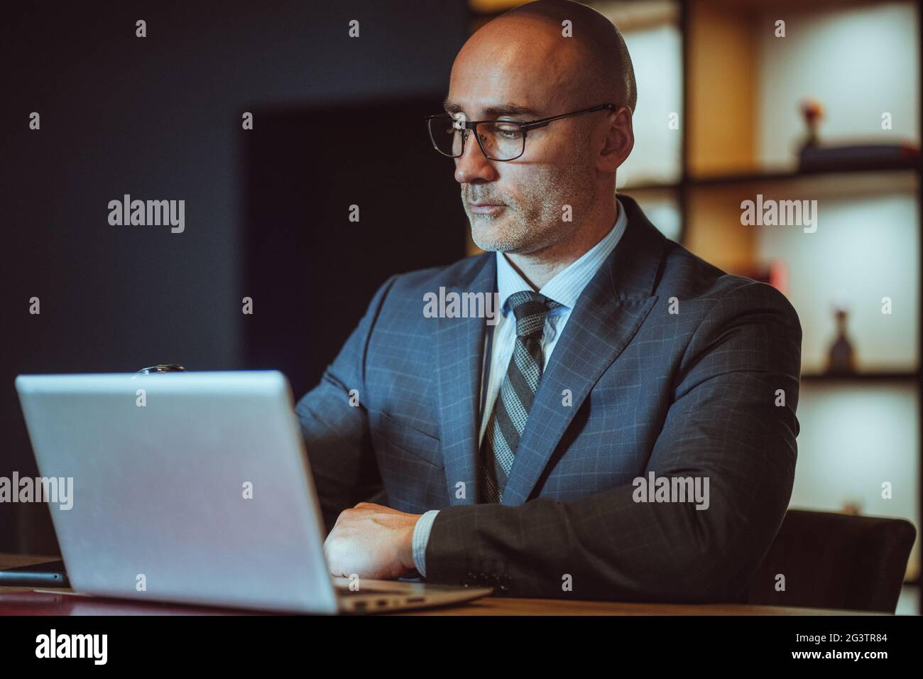 CEO di media età, sicuro e calvo, che lavora su un computer portatile indossando una suite aziendale in un ufficio moderno. Bell'uomo audace che lavora su l Foto Stock