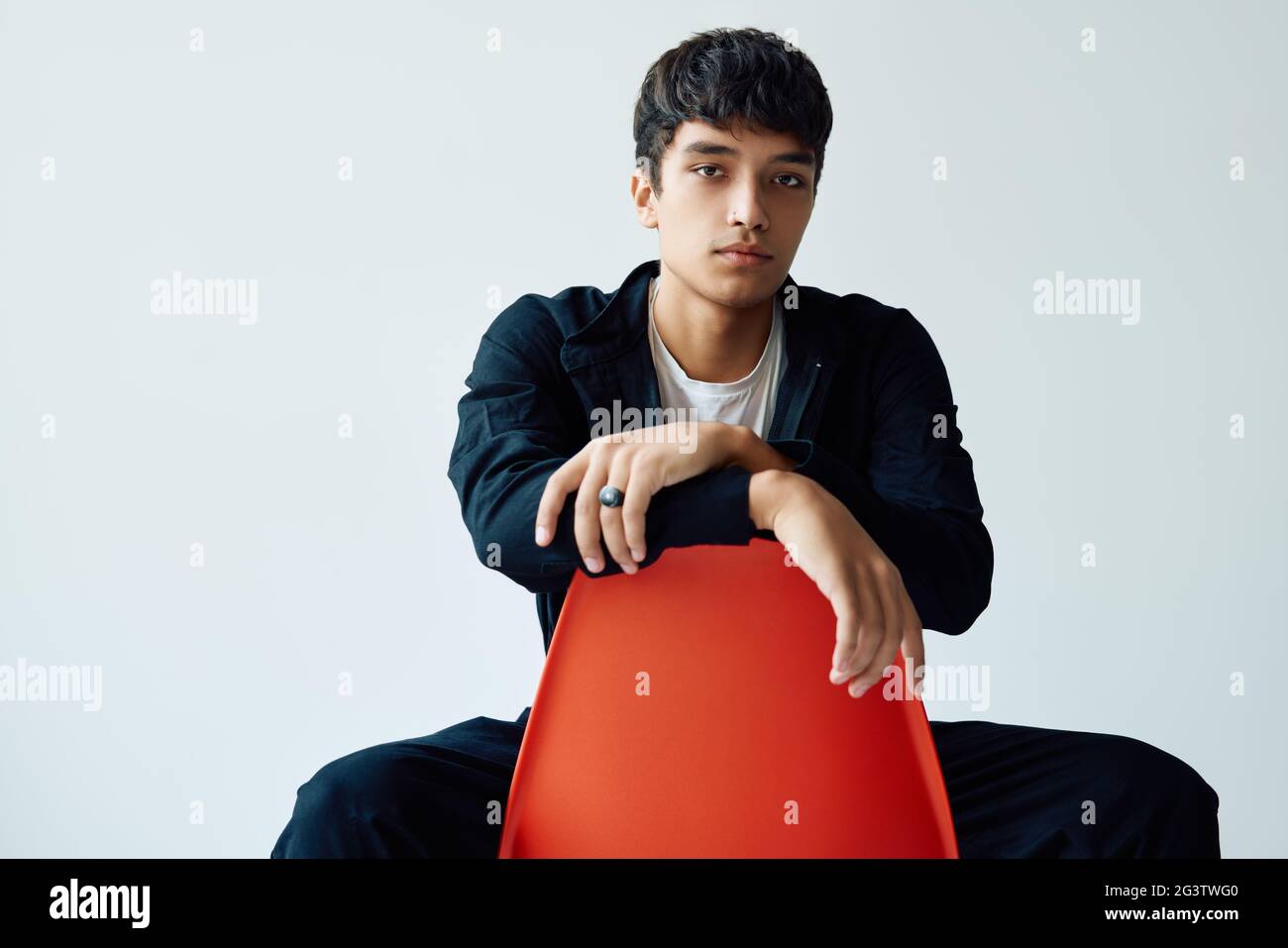 Elegante bel giovane uomo che posa in studio seduto su una sedia che guarda alla macchina fotografica Foto Stock