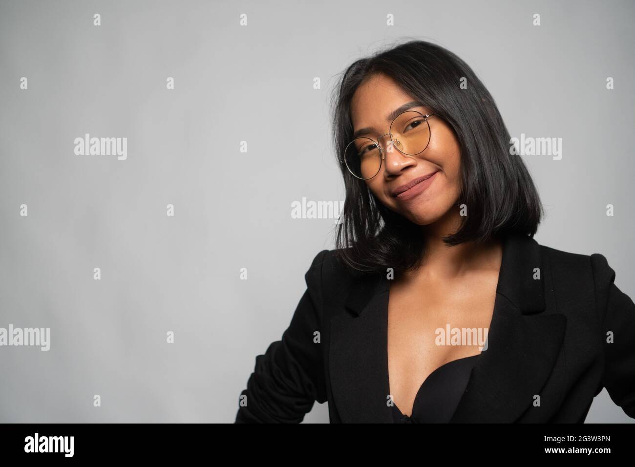 Attraente giovane donna asiatica in elegante blazer nero e vetri isolati su parete grigio chiaro Foto Stock